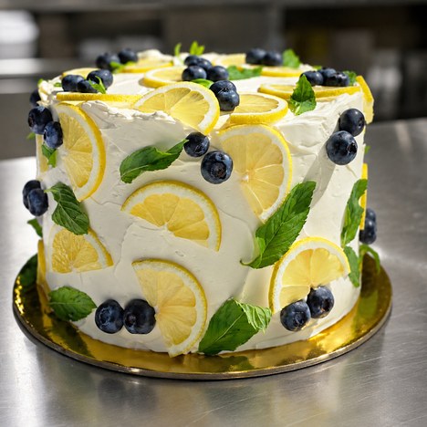 Lemon blueberry layer cake frosted in white with lemon slices, blueberries and mint